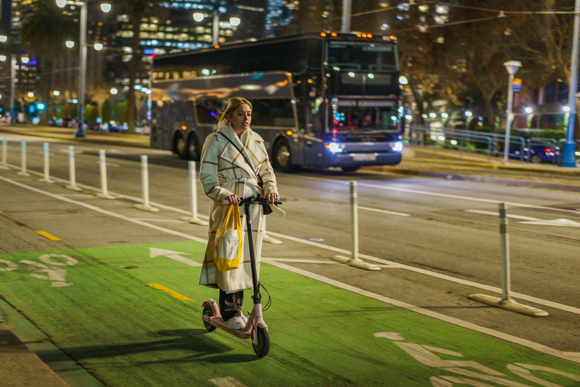 Young woman riding electric kick scooter on a city bike lane at night